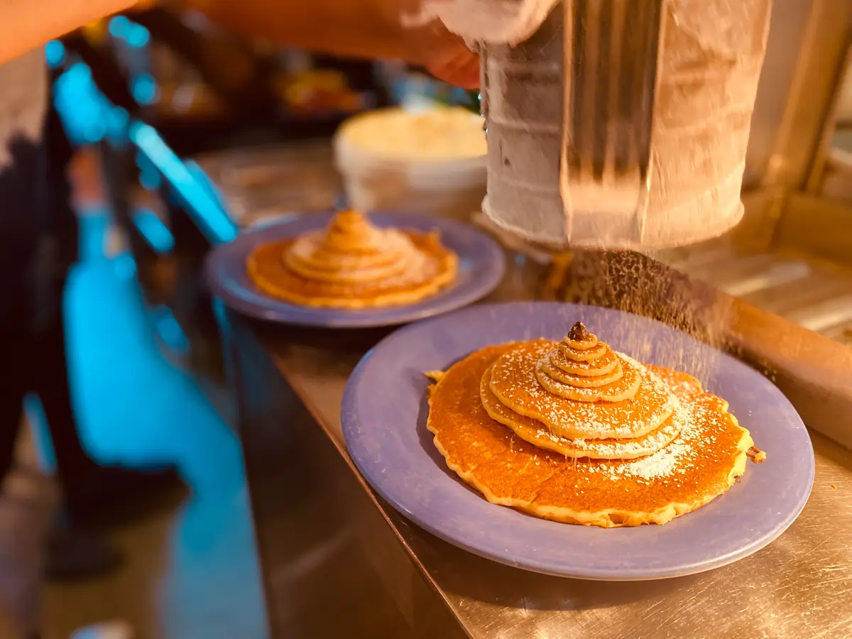 A stack of pancakes being powdered with sugar.